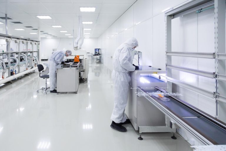 Interdição de processos industriais sensíveis: trabalhadores de fábrica em trajes de laboratório brancos; ambiente limpo, branco.